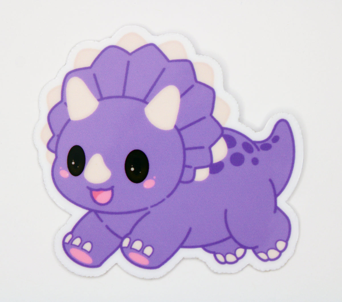 A die-cut vinyl sticker of a cute purple cartoon Triceratops dinosaur, shown on a plain white background.