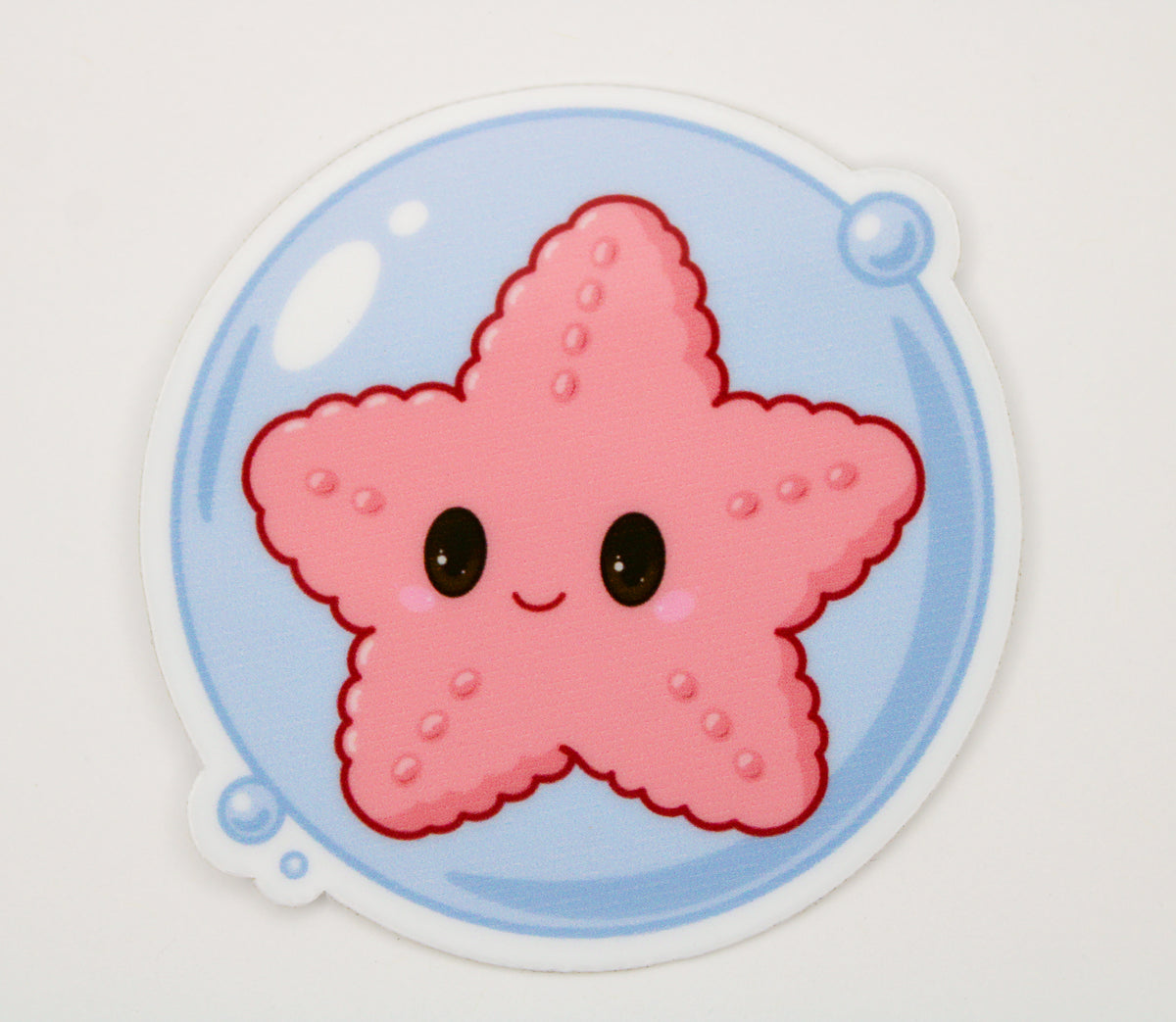 A die-cut sticker featuring a cute pink starfish character with large black eyes inside a light blue circular bubble with small blue bubbles, shown on a plain white background.