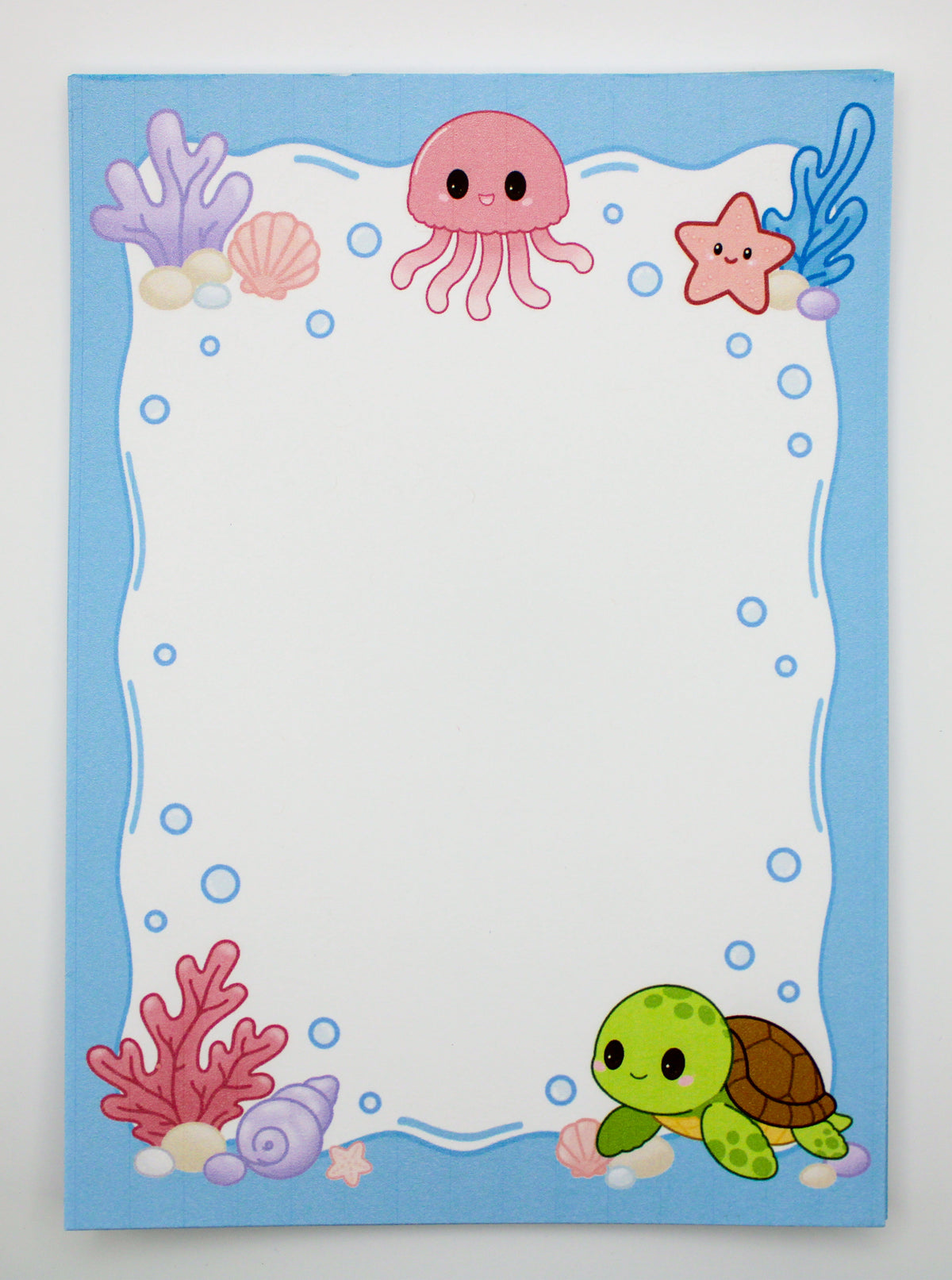 A square stationery card or notepad with a cute underwater theme, featuring a light blue border decorated with a pink jellyfish, purple coral, a green turtle, a pink starfish, and blue bubbles on a white writing area.