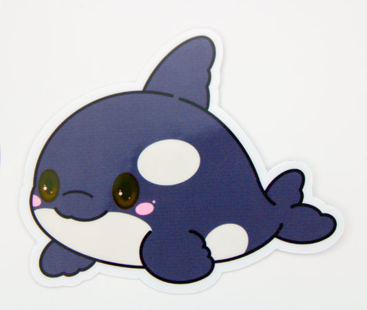 A cute cartoon orca whale sticker with a white border, featuring dark blue and white coloring, pink cheeks, and large brown eyes on a plain white background.