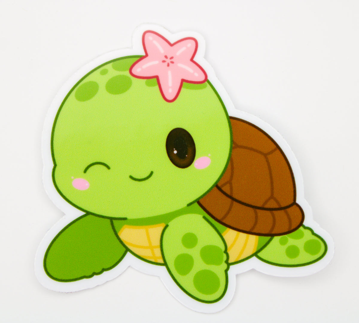 A cartoon sea turtle sticker with a pink starfish on its head, winking with one eye, on a white background.