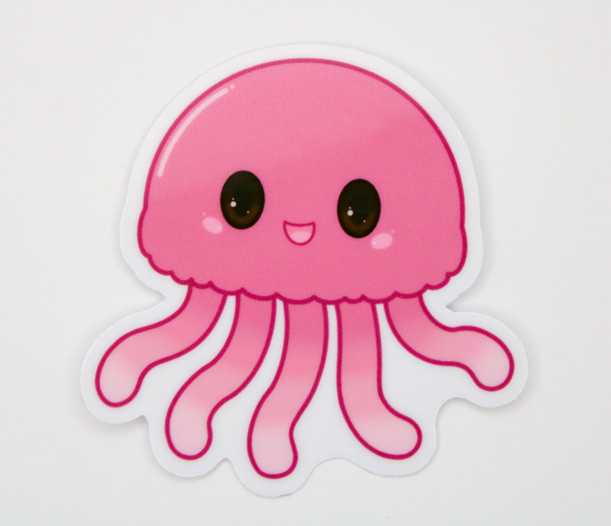 A die-cut vinyl sticker featuring a cute, cartoon-style pink jellyfish with large black eyes and a smiling mouth, shown on a plain white background.