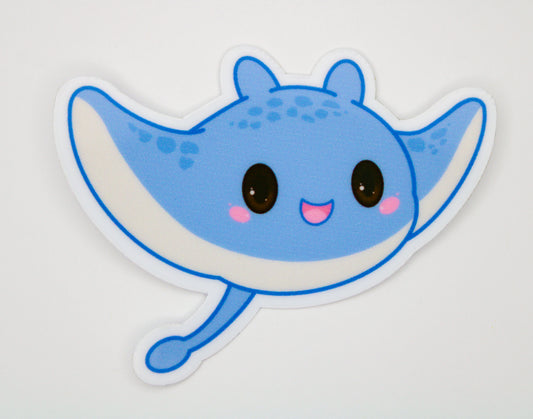 A cute cartoon manta ray sticker or decal in light blue and white with pink cheeks and black eyes, shown on a plain light background.