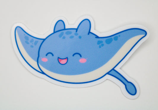 A die-cut vinyl sticker of a cute blue cartoon manta ray with pink cheeks and a smiling mouth, shown on a plain light gray background.