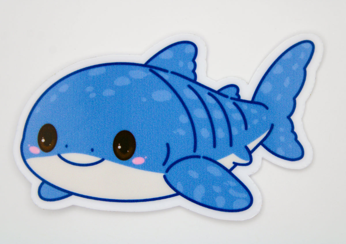 A die-cut vinyl sticker of a cute, cartoonish blue shark with a white belly, pink cheeks, and black outlines, shown on a plain white background.