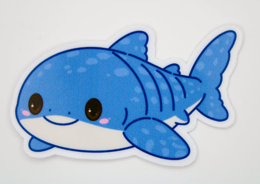 A die-cut vinyl sticker of a cute, cartoonish blue shark with a white belly, pink cheeks, and black outlines, shown on a plain white background.