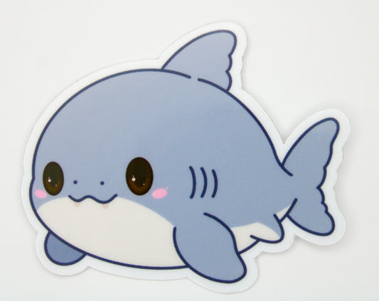 A die-cut vinyl sticker of a cute, cartoonish baby shark in light blue and white with pink cheeks, shown on a plain white background.