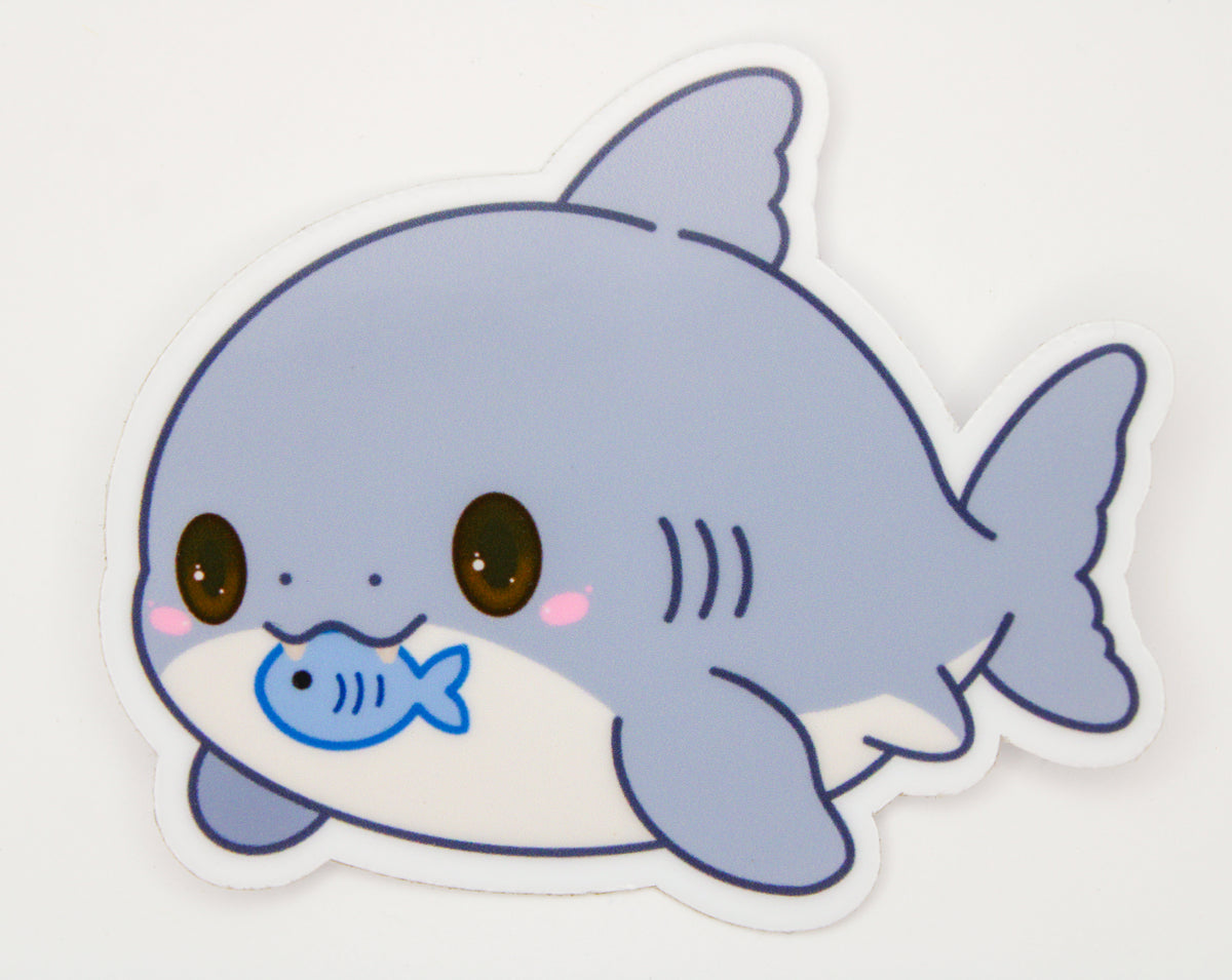 A die-cut sticker featuring a cute cartoon shark with a blue fish in its mouth, shown on a plain white background.