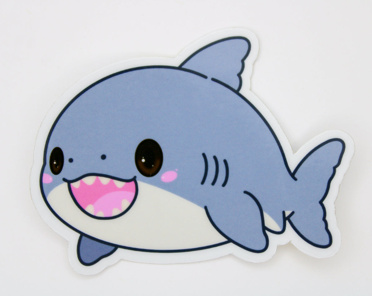 A die-cut vinyl sticker of a cute cartoon baby shark, featuring a light blue-gray body, white underbelly, pink mouth, and large brown eyes, shown on a plain white background.