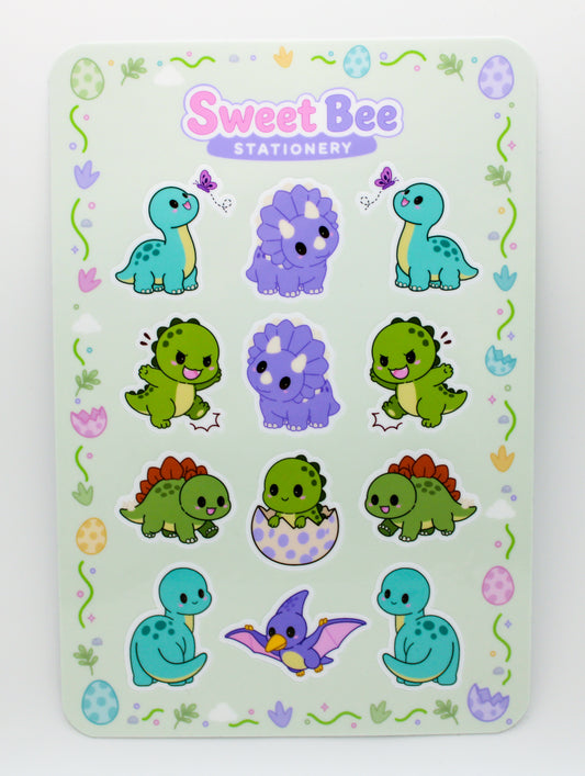 A Sweet Bee Stationery sticker sheet featuring cute cartoon dinosaurs in various poses and colors, including teal, purple, green, and red, on a pale mint green background with a decorative border.