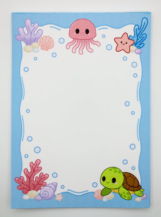 A square stationery card or notepad with a cute underwater theme, featuring a light blue border decorated with a pink jellyfish, purple coral, a green turtle, a pink starfish, and blue bubbles on a white writing area.