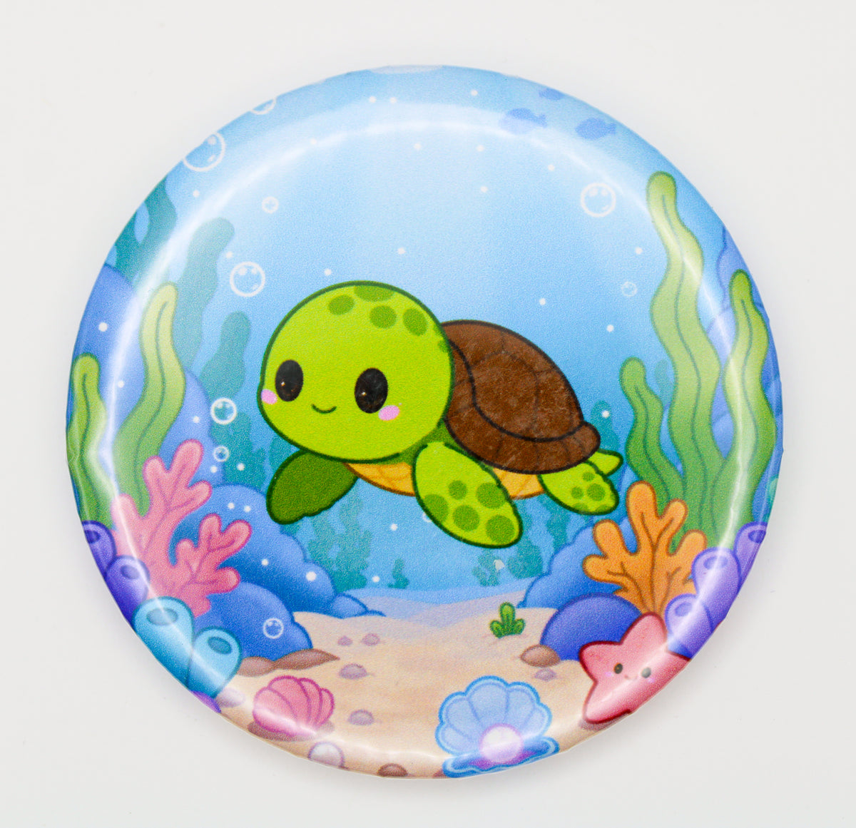A round pinback button badge featuring a cute cartoon sea turtle swimming underwater, surrounded by colorful coral, seaweed, bubbles, and a sandy ocean floor on a light gray background.
