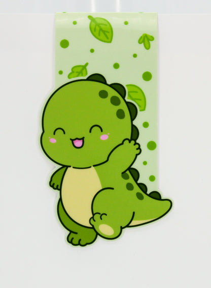 A cute cartoon dinosaur sticker or decal in shades of green, shown against a light green patterned background with green leaves and dots.